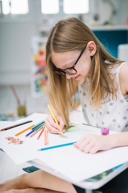 Glimlachend meisje met potlood het schilderen op papier bij lijst in ruimte