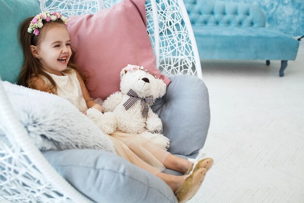 Glimlachend meisje zit in hangende stoel met blauwe en roze kussens