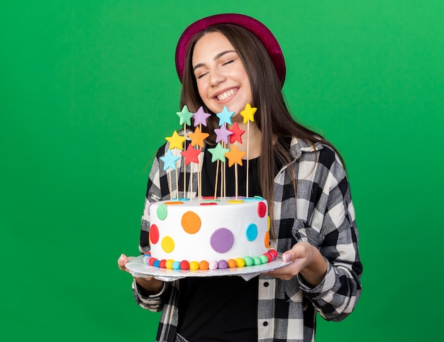 Glimlachend met gesloten ogen jong mooi meisje met feestmuts met cake