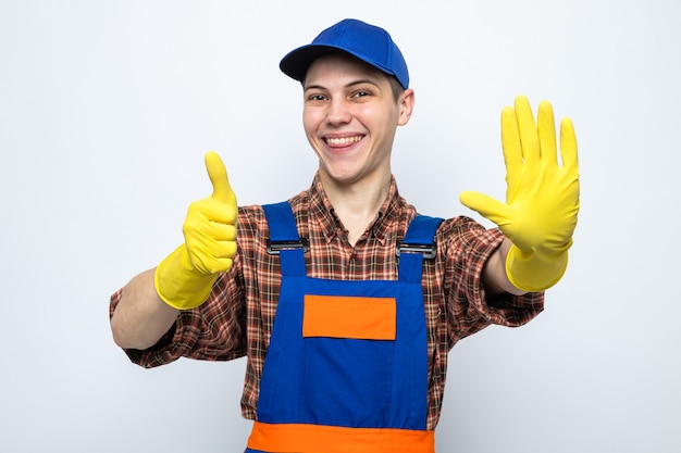 Glimlachend met stopgebaar zijn duim omhoog jonge schoonmaakster die uniform en pet met handschoenen draagt