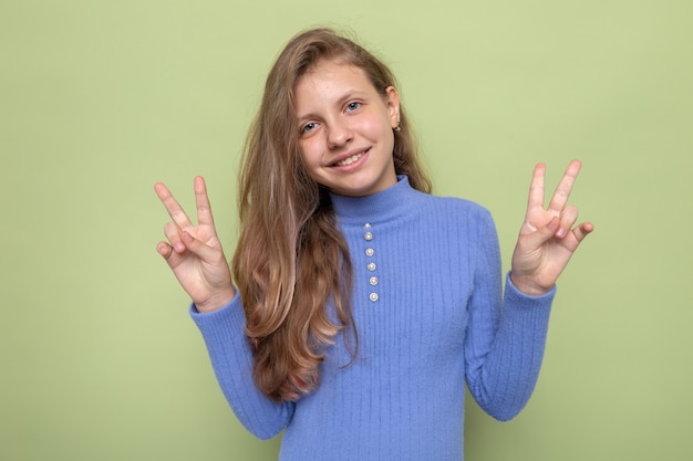 Gratis foto glimlachend met vredesgebaar, mooi klein meisje met blauwe trui