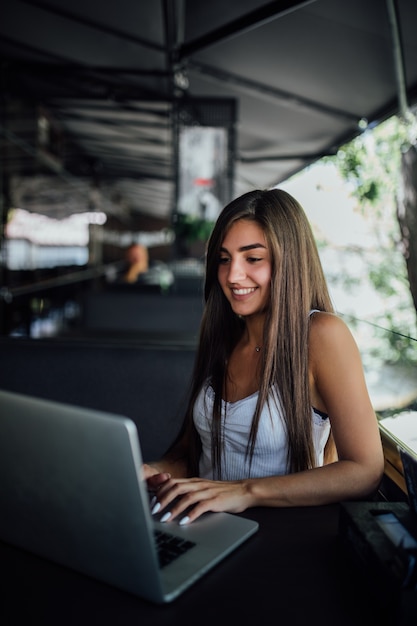 Glimlachend modelmeisje werkt op haar laptop op het terras van cafe daytilme