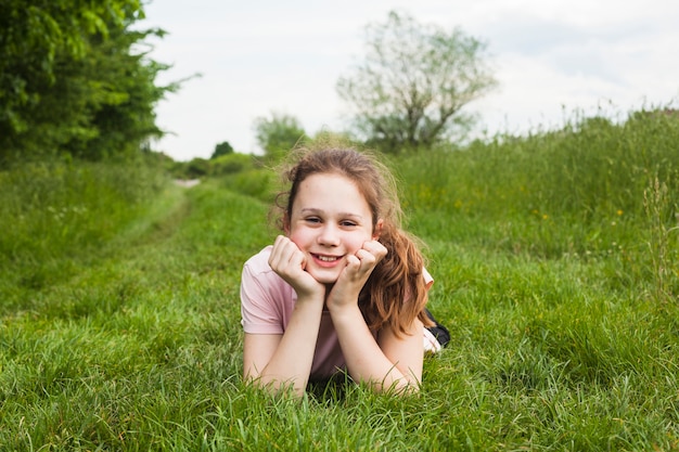 Glimlachend mooi meisje dat op groen gras bij park ligt