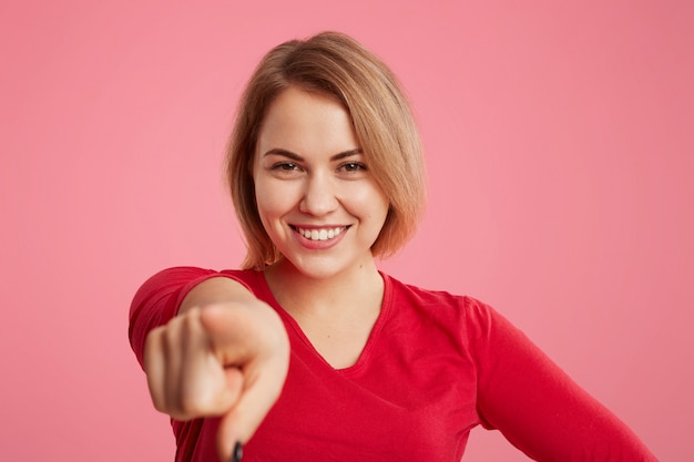 Gratis foto glimlachend mooie jonge vrouw heeft een brede stralende glimlach geeft aan met je wijsvinger, maakt keuze