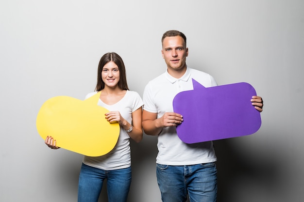 Glimlachend paar dat gele en blauwe praatjewolken in hun handen houdt die op witte achtergrond worden geïsoleerd