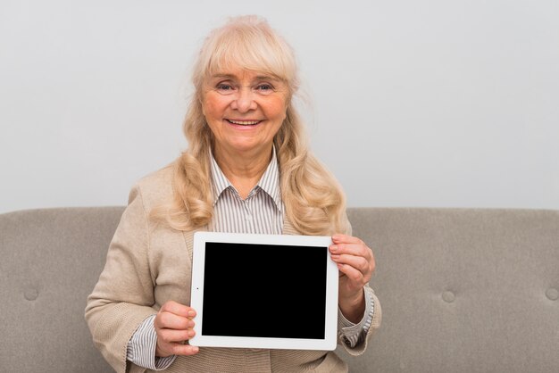 Glimlachend portret van blonde hogere vrouw die digitale tablet met het lege scherm tonen