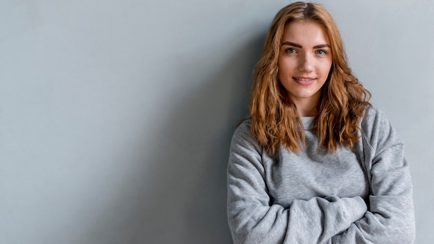 Glimlachend portret van een jonge vrouw die camera tegen grijze muur bekijkt