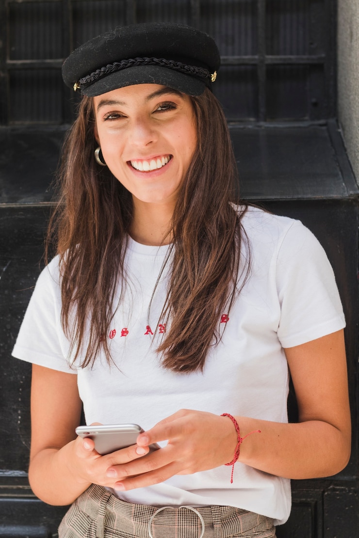 Gratis Foto glimlachend portret van een jonge vrouw die mobiele telefoon houdt die ter beschikking camera bekijkt