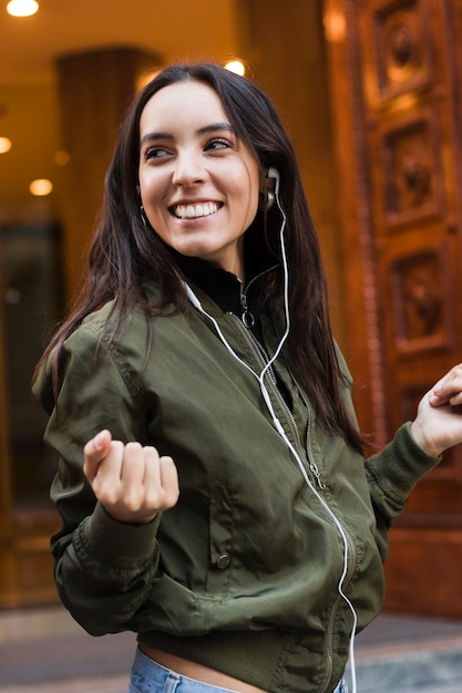 Gratis foto glimlachend portret van een jonge vrouw die terwijl het luisteren van muziek op telefoon geniet van