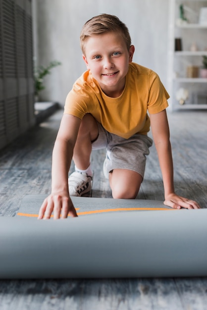 Glimlachend portret van een jongen die oefeningsmat plaatsen op vloer