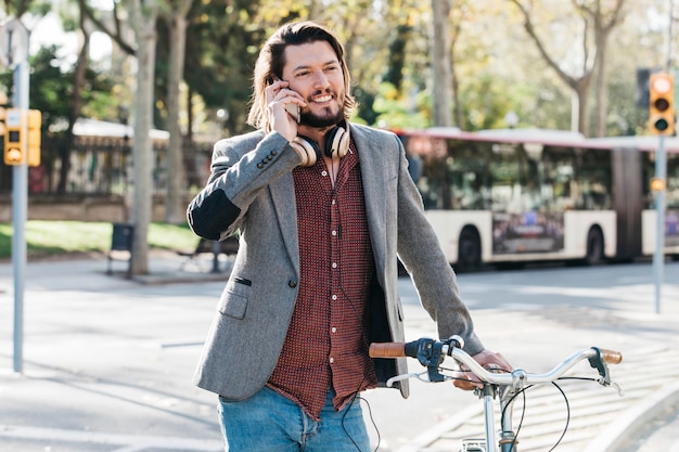 Glimlachend portret van een knappe mens die op mobiele telefoon spreekt die zich met fiets bevindt
