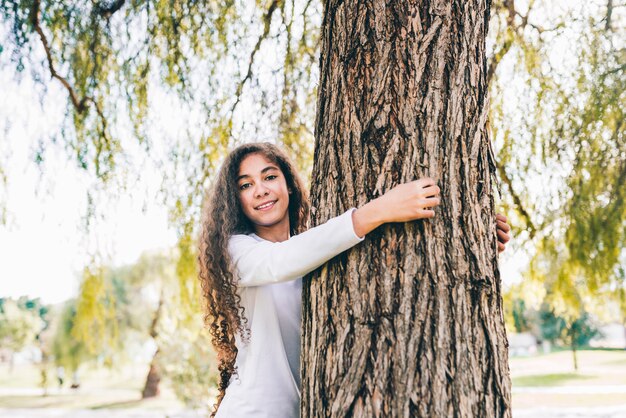 Gratis foto glimlachend portret van een meisje die boomboomstam in het park koesteren