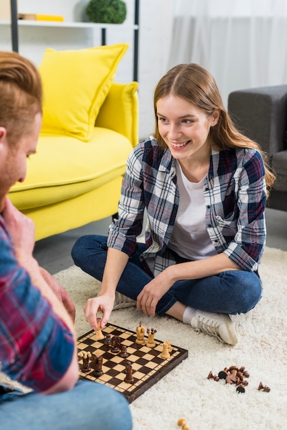 Gratis foto glimlachend portret van jonge vrouwenzitting met haar vriend het spelen schaak thuis