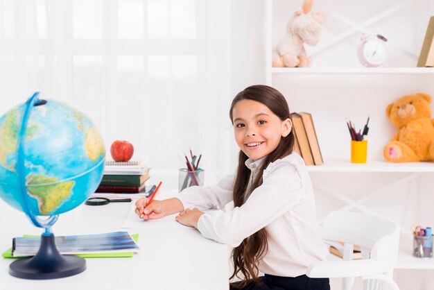 Glimlachend schoolmeisje in een uniform thuis studeren