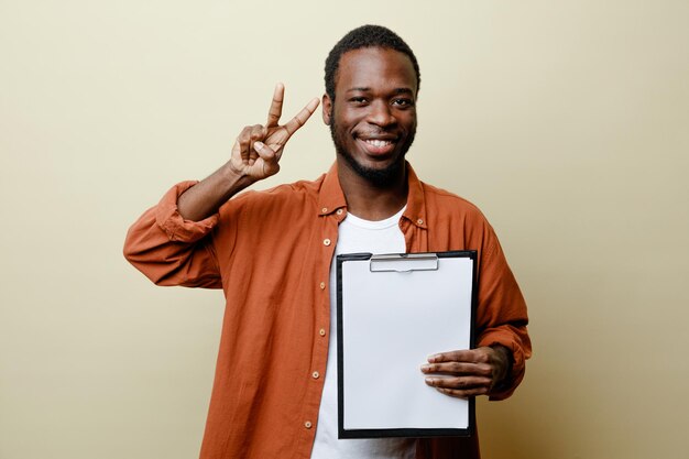 Glimlachend toont vredesgebaar jonge Afro-Amerikaanse man met klembord geïsoleerd op een witte achtergrond