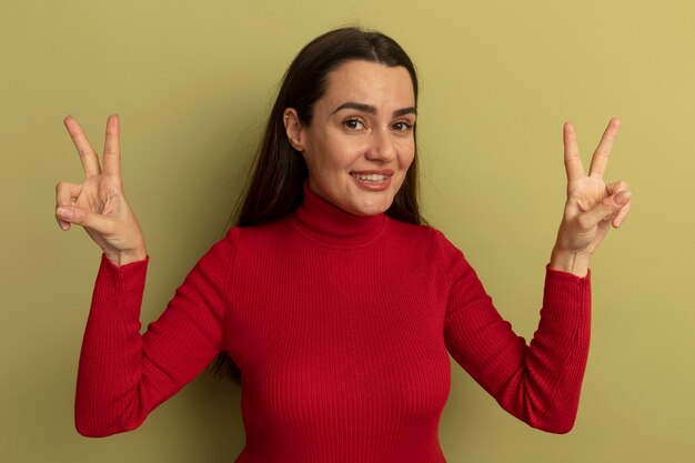 Glimlachend vrij blanke vrouw gebaren overwinning handteken met twee handen op olijfgroen