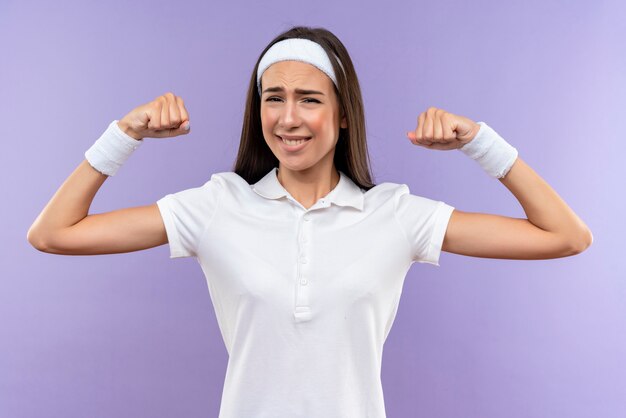 Glimlachend vrij sportief meisje met hoofdband en polsbandje gebaren sterk geïsoleerd op paarse ruimte