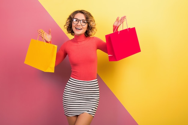 Gratis foto glimlachende aantrekkelijke opgewonden vrouw in stijlvolle kleurrijke outfit met boodschappentassen