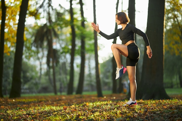 Gratis foto glimlachende actieve vrouw die fitnessoefeningen doet bij park at