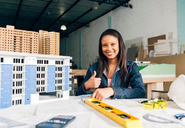 Glimlachende Afrikaans-Amerikaanse vrouw die duim toont dichtbij model van de bouw