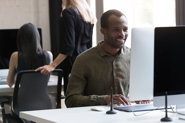 Glimlachende Afrikaanse Amerikaanse zakenman die aan zijn computer werkt