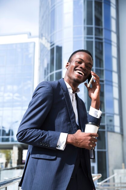 Glimlachende Afrikaanse jonge zakenman voor de collectieve bouw die op mobiele telefoon spreekt