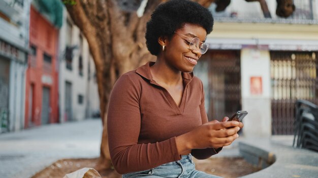 Glimlachende Afrikaanse vrouw in casuals chatten met vrienden aan de telefoon