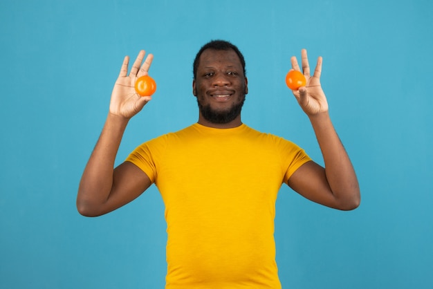 Glimlachende Afro-Amerikaanse man met een mandarijn in beide handen, staat over blauwe muur.