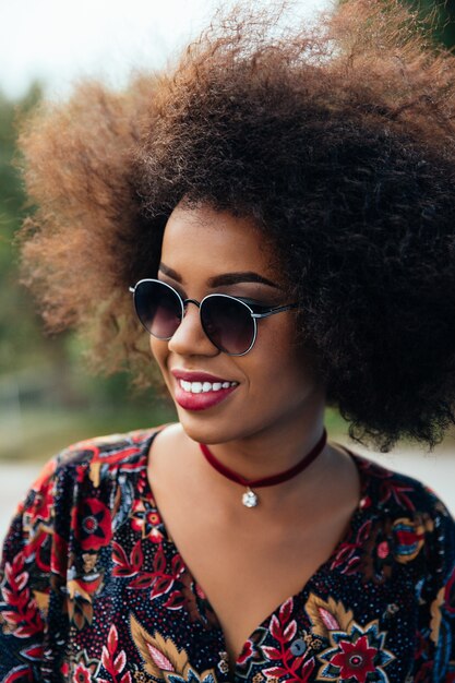 Glimlachende Afro-Amerikaanse vrouw met kort volumineus haar, die zonnebril draagt.