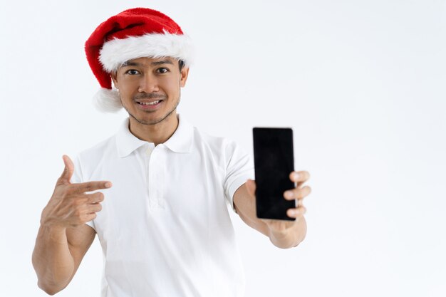 Glimlachende Aziatische mens die Kerstmanhoed draagt en op smartphone richt
