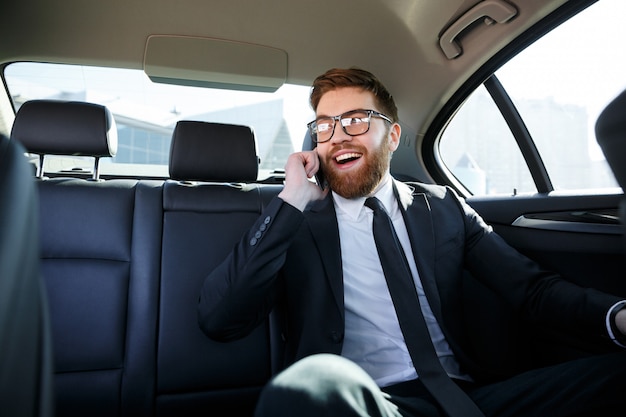 Glimlachende bebaarde zakenman in brillen praten op mobiele telefoon