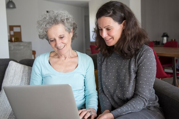 Glimlachende bejaarde en haar dochter die op laptop doorbladeren