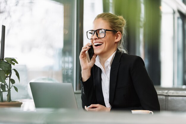 Glimlachende blonde bedrijfsvrouw die door mobiele telefoon spreekt