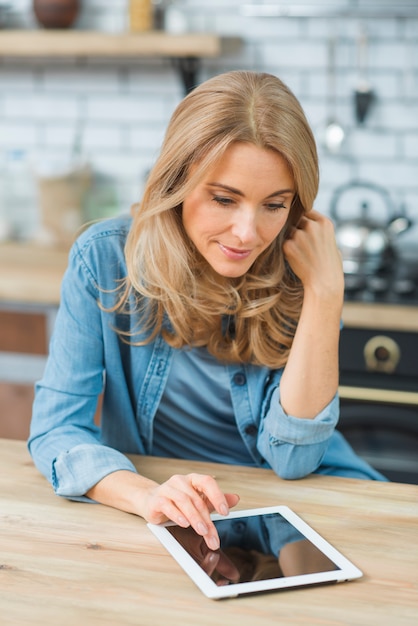 Gratis foto glimlachende blonde jonge vrouw die de aanrakingsgevoelige digitale tablet op lijst gebruiken