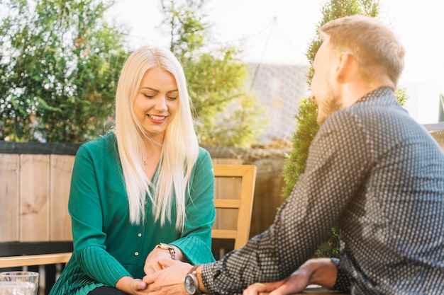 Glimlachende blonde jonge vrouw die de hand van zijn vriend houdt