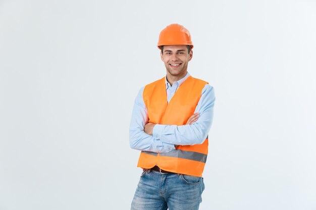 Glimlachende bouwingenieur poseren met gekruiste armen. Geïsoleerd over grijze achtergrond.