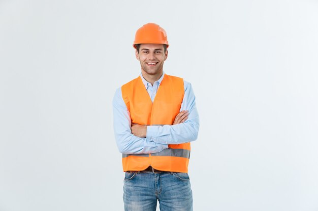 Glimlachende bouwingenieur poseren met gekruiste armen. Geïsoleerd over grijze achtergrond.