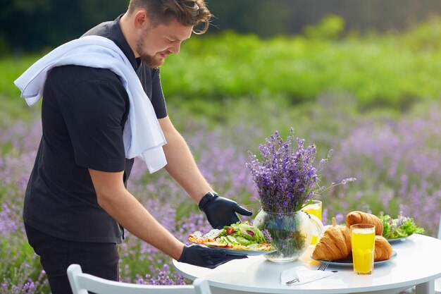 Glimlachende chef-kok serveert eten op tafel in lavendelveld