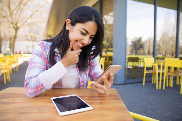 Glimlachende dame die tablet en smartphone op openluchtkoffie gebruikt