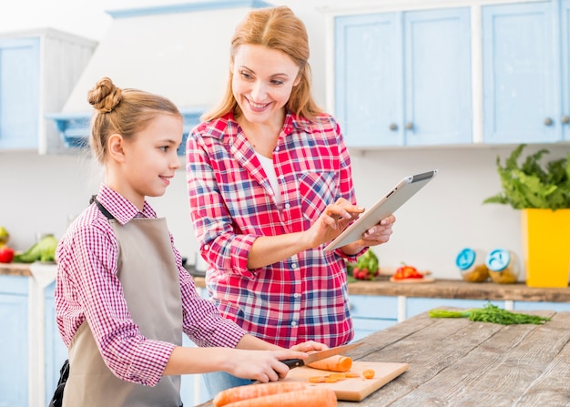 Gratis foto glimlachende dochter die haar moeder bekijkt die recept op mobiele telefoon toont