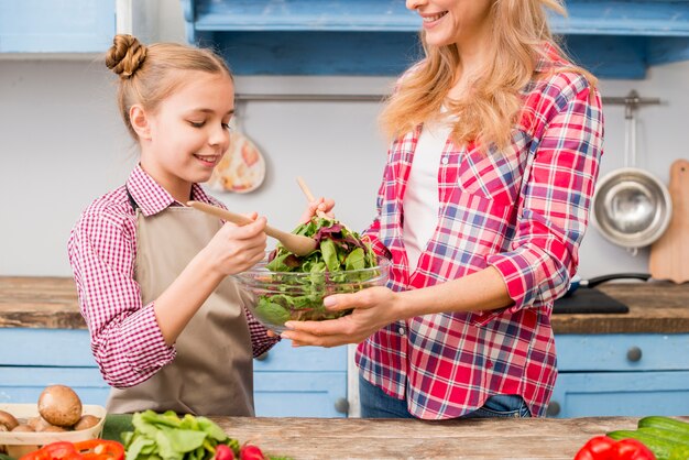 Glimlachende dochter en moeder die de bladgroentensalade in de keuken voorbereiden