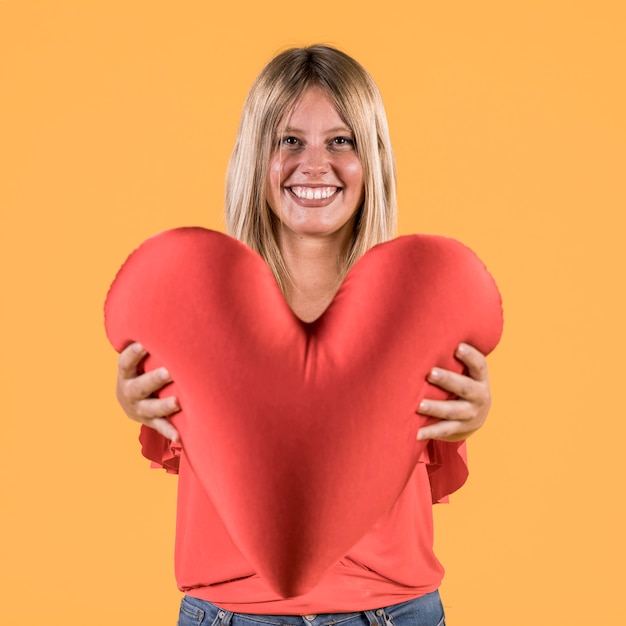 Gratis foto glimlachende dove vrouw die rood kussen van de hartvorm geeft aan iemand