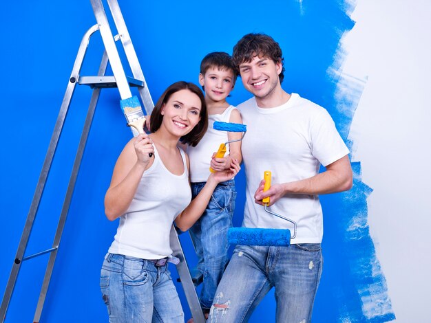 Glimlachende en gelukkige familie met verfborstels die renovatie doen - binnenshuis