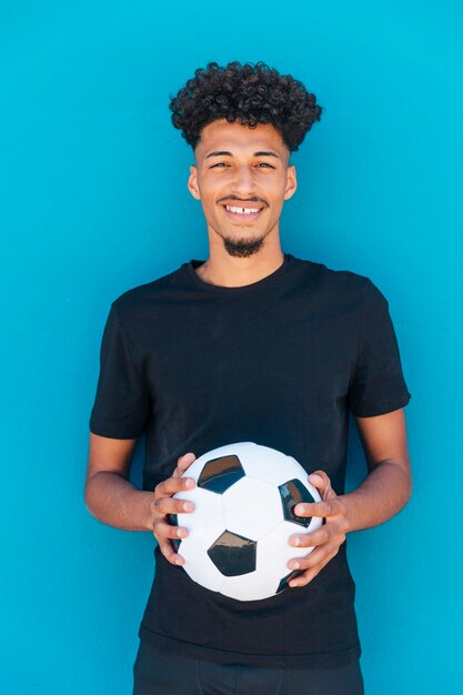 Glimlachende etnische kerel die zich met voetbal bevindt