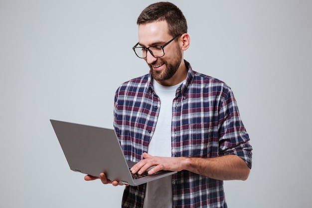 Glimlachende gebaarde mens in oogglazen die laptop met behulp van