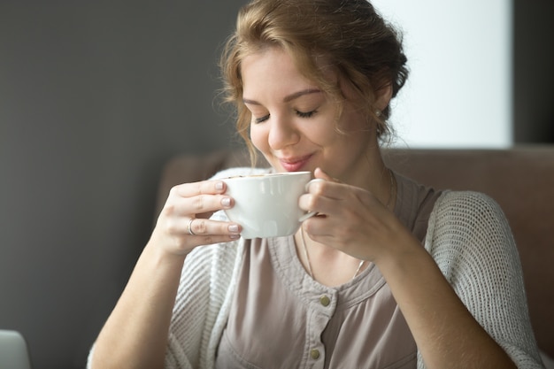 Glimlachende gelukkige vrouw drinkende aromatische koffie met gesloten ogen