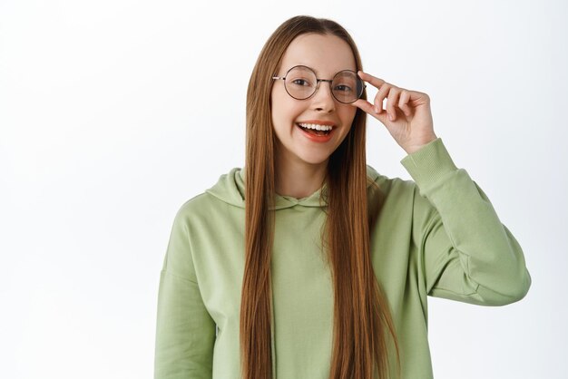 Glimlachende gelukkige vrouw zette een bril op en zag er zelfverzekerd en slim uit over een witte achtergrond in een casual hoodie