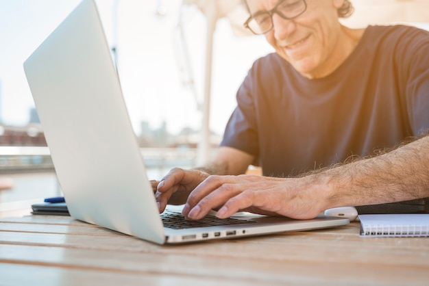 Glimlachende hogere mens die laptop met behulp van bij openluchtcafã