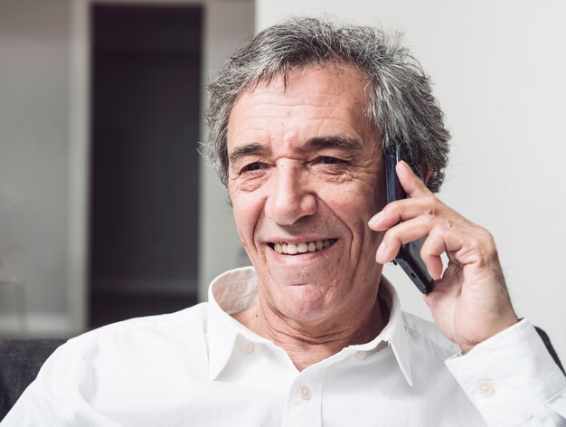 Glimlachende hogere zakenman die op smartphone spreken