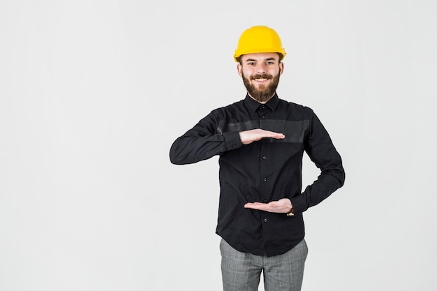 Glimlachende ingenieur die het gele bouwvakker gesturing dragen